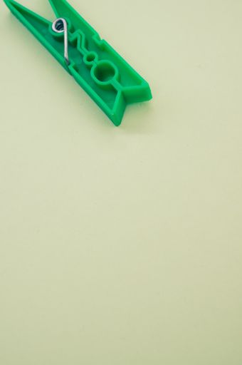 A vertical shot of green plastic clothespin isolated on a light background