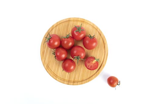 Fresh cherry tomatoes on a round wooden tray isolated on a white background