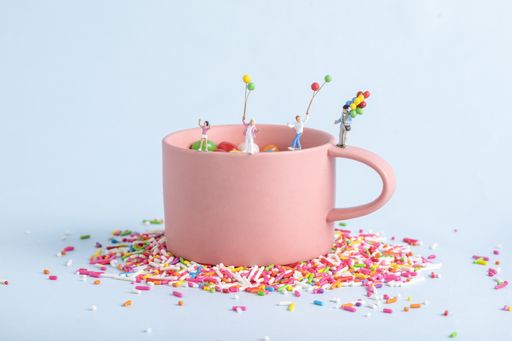 A closeup shot of human figurines with balloons playing in a pink cup with sprinkles