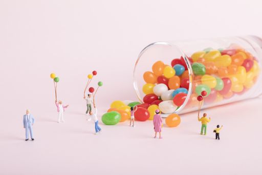 A closeup shot of small cute human figurines playing with balloons near jelly beans