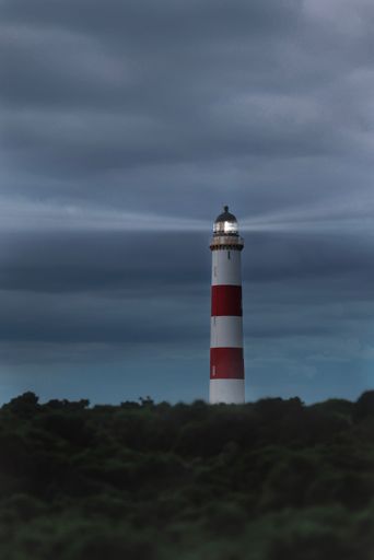A vertical shot of red and white lighthouse on coast under gloomy cloudy sky, North Scotland