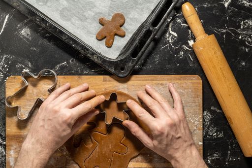 a top view of two hands making gingerbread man cookies and cookie cutters