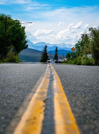 A vertical shot of an empty highway amid trees under the blue sky