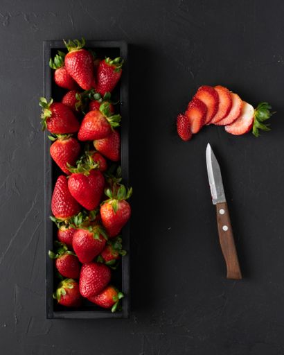 An overhead shot of fresh harvested strawberries in a black wooden box