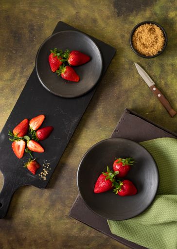 A vertical shot of slices of red, fresh strawberries on a black wooden board