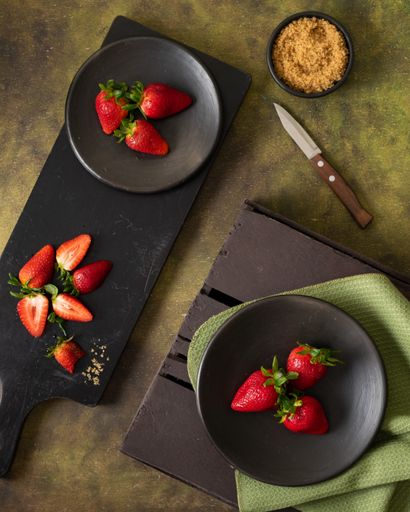 A top view of ripe strawberries on boards on the table with a knife and a bowl of muesli on it