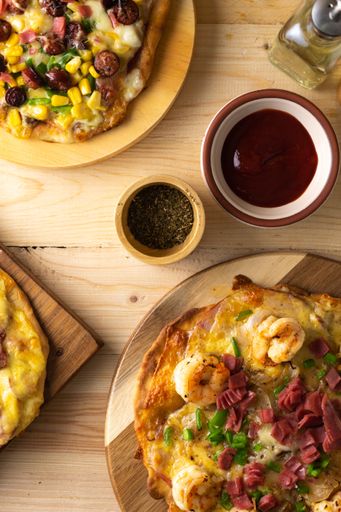 A vertical shot of homemade traditional pizzas with different toppings on a wooden table