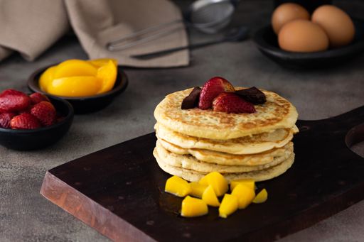 A closeup of delicious pancakes with mangoes and strawberries on a board on the table