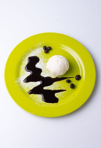 An overhead shot of a scoop of vanilla ice cream on a yellow plate with powdered sugar, chocolate syrup