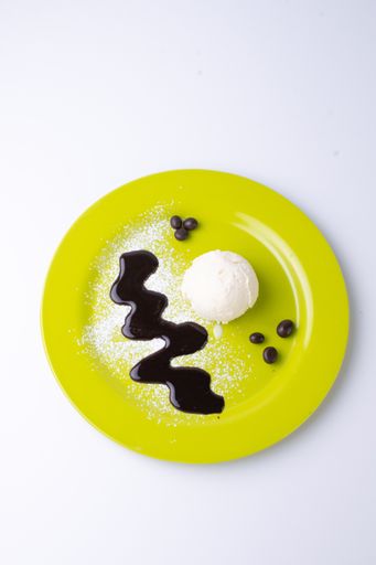 A vertical shot of a ball of vanilla ice cream with melted chocolate on a green plate isolated on a gray background