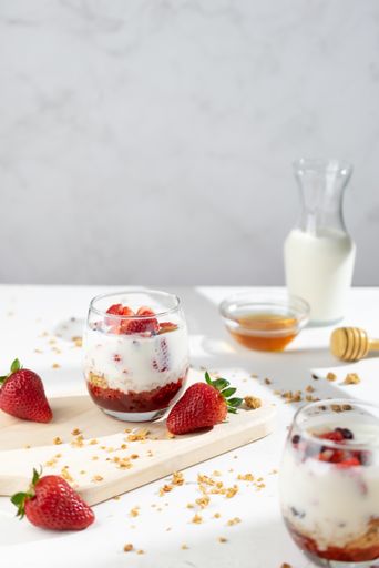 A vertical shot of delicious muesli with strawberries, yogurt, and honey in glasses on the table