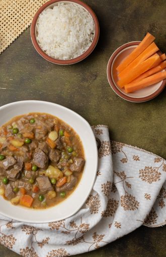 A vertical shot of a bowl of delicious stew with beef, beans, potatoes, and carrots on the table