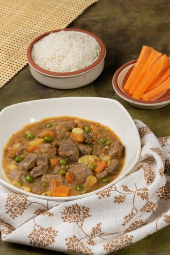 A vertical shot of a bowl of delicious stew with beef, beans, carrots, and potatoes on the table