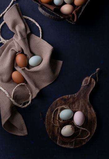 A top view of colorful eggs for Easter on a wooden board and fabric on the table