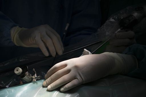 A closeup shot of a pair of hands with surgical instruments on the dark background