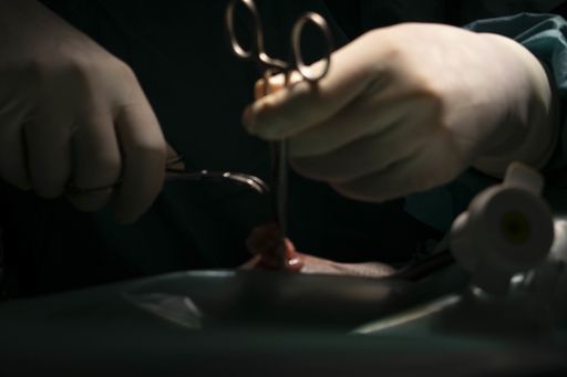 A closeup shot of a pair of hands operating with surgical instruments on the dark background