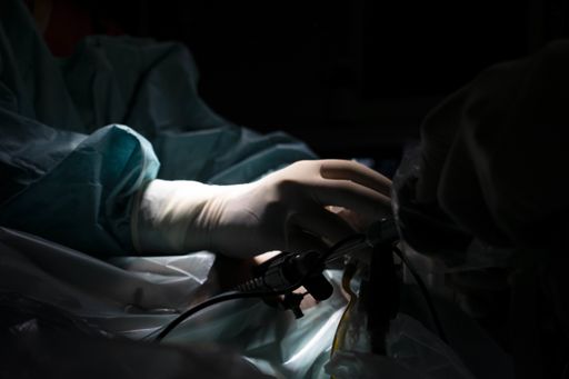A closeup shot of a hand during a surgical process with surgical instruments on the dark background