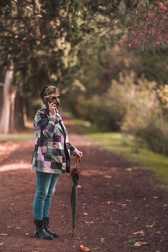 A stylish middle-aged female wearing a face mask, holding an umbrella and talking on phone