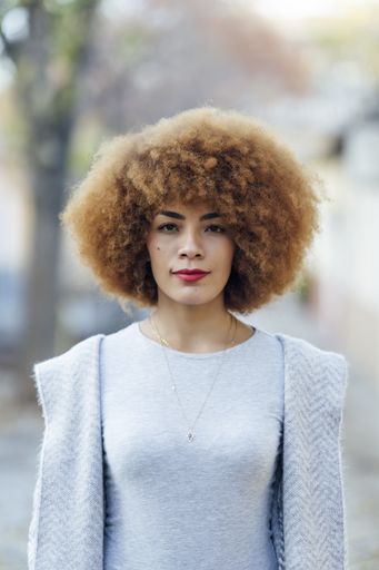 A shallow focus of a young Hispanic female with curly hair wearing a gray cardigan with a sweater