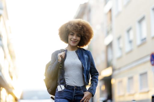 A shallow focus of a young Hispanic female with a backpack wearing a denim jacket and walking down the street