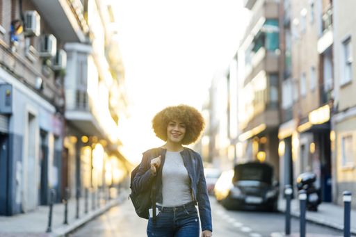 A shallow focus of a young Hispanic female with a backpack wearing a denim jacket and walking down the street