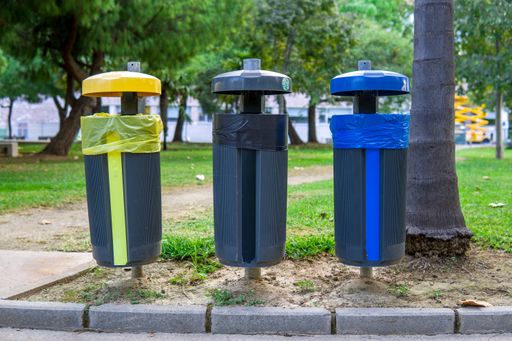 Eco Friendly Recycle Bins of Different Colors in a Park with a Background of Grass and Trees.