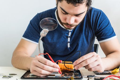 A repairman testing the electric circuit of a tablet. Young repairman of phones and tablets. Smartphone repair.
