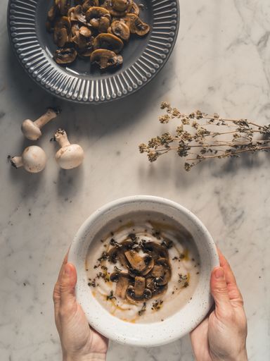 A top view of woman hands holding a bowl of mushroom soup