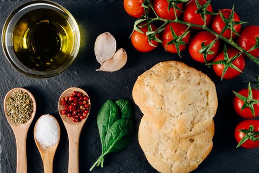 A top view closeup of the oil, bread, fresh cherry tomatoes, herbs, and spices on the table