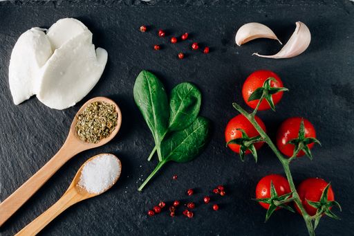 A top view closeup of the fresh cherry tomatoes, mozzarella, spices, garlic, and spinach