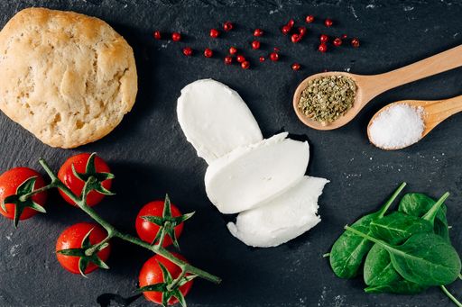 A top view closeup of the fresh cherry tomatoes, mozzarella, spice, bread, garlic, and spinach