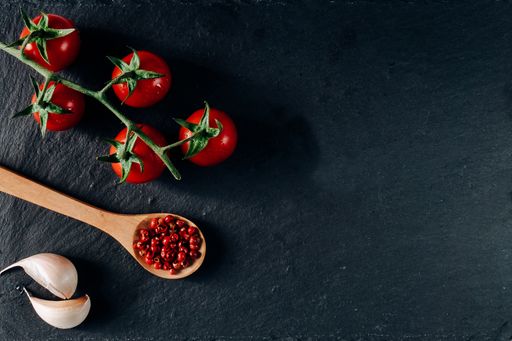 An overhead shot of cherry tomatoes, garlic, and wooden spoon with spice on a dark background