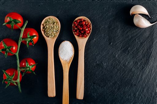 An overhead shot of cherry tomatoes, garlic, and wooden spoons with spice on a dark background