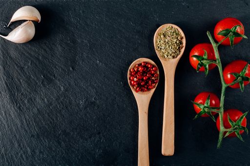 An overhead shot of cherry tomatoes, garlic, and wooden spoons with spice on a dark background