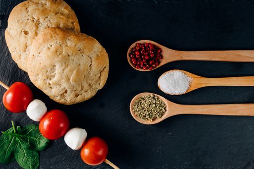 An overhead shot of colorful food spices, bread, and mozzarella on a dark background