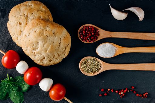 An overhead shot of colorful food spices, bread, garlic, and mozzarella on a black background