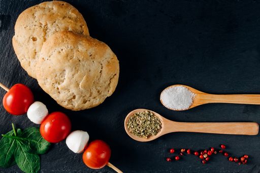 An overhead shot of bread, garlic, herbs, and mozzarella-tomato sticks on a dark background