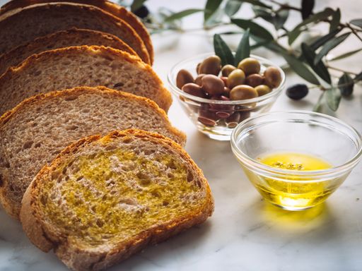 A closeup shot of slices of bread with extra virgin oil near glass bowls filled with oil and olives