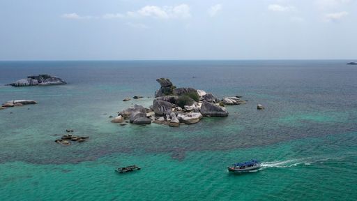 An aerial shot of a rocky island near a boat in the sea