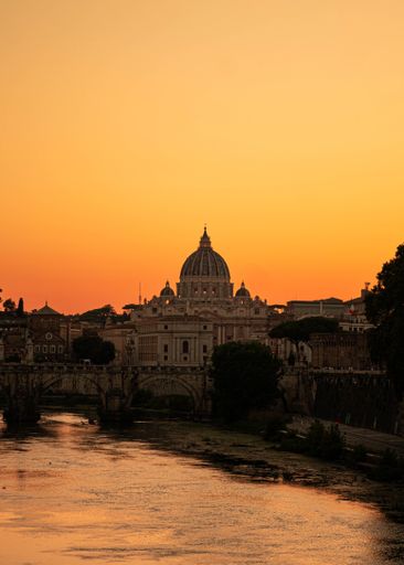 A vertical shot of a river with St. Peter's Basilica building in the background during sunset, Vatican