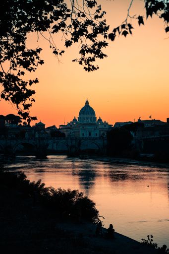 A vertical shot of a river with St. Peter's Basilica building in the background during sunset, Vatican