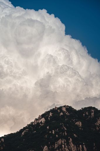 A scenic view of a mountain range with white, fluffy clouds suspended in the sky above