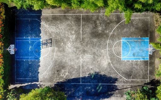 An aerial view of an empty basketball court surrounded by lush greenery