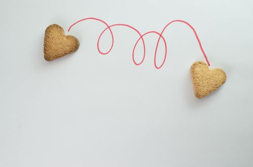 A flat lay of heart shaped cookies connected with a red thread - concept of loving hearts