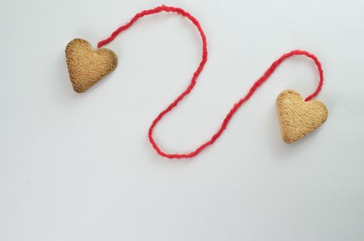 A flat lay of heart shaped cookies connected with a red thread - concept of loving hearts