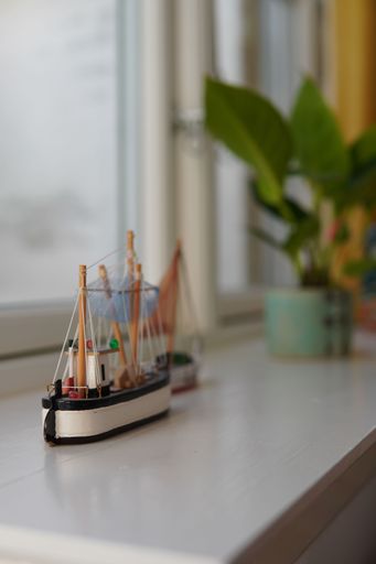 A vertical closeup of a miniature boat toy on a windowsill with plants in the blurred background