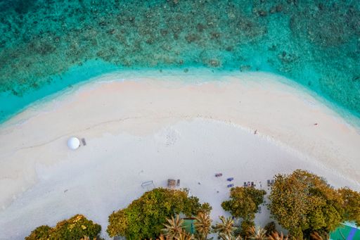 A beautiful bird's eye view of a white beach with bright turquoise tides washing over it in Kamadhoo, Maldives
