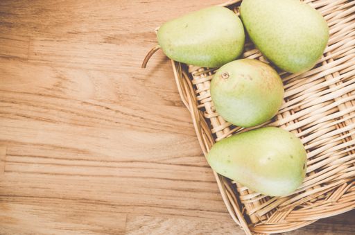A top view of some green pears on a wicker basket and wooden surface