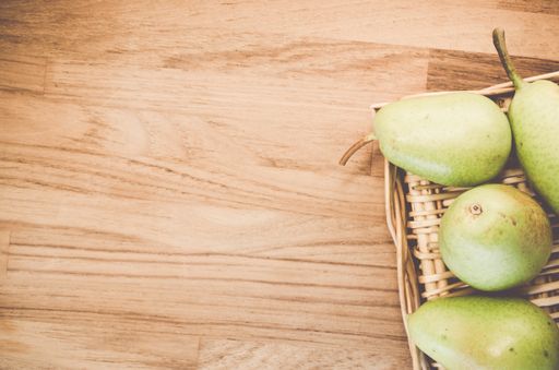 A top view of green pears on a wicker basket and wooden surface