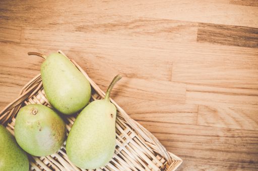 A top view of green pears on a wicker basket and wooden surface